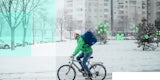 Delivery person riding his bike through a snowy city street.